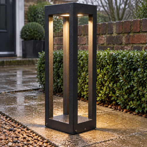 Black aluminium LED bollard light standing beside a wet garden path in the drizzle