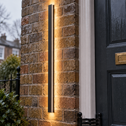 Minimalist black linear LED outdoor wall sconce beside a British front door in drizzle
