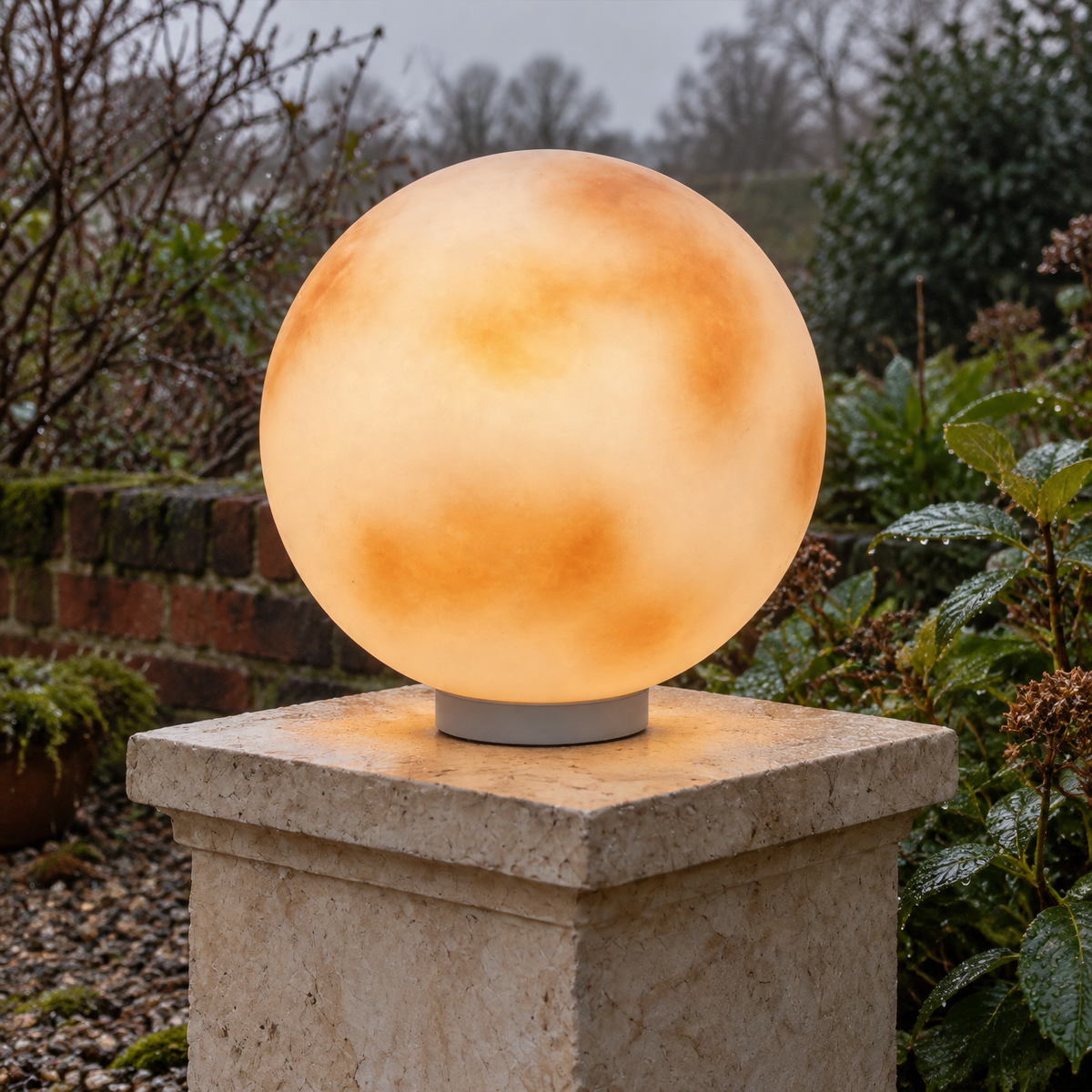 Moon shaped stone pillar light glowing on a pedestal in a misty British garden