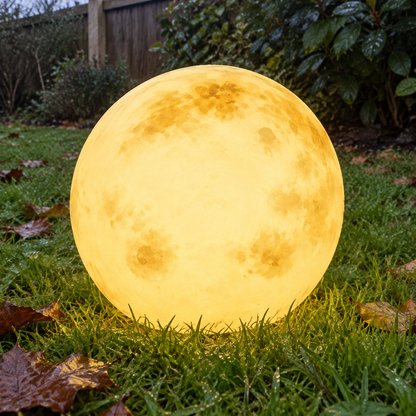 Glowing moon ball garden light resting on damp grass in a British back garden