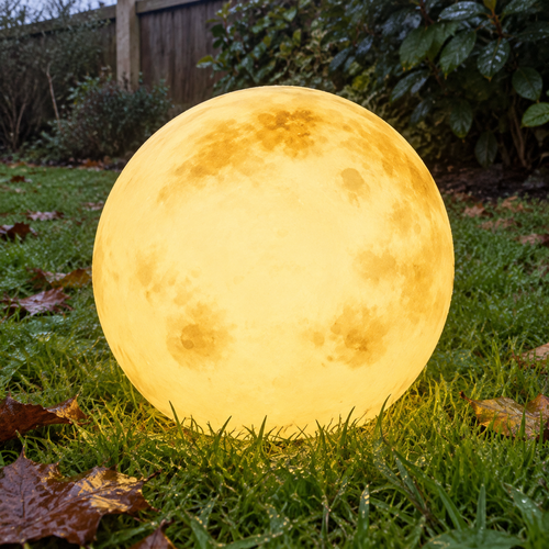 Glowing moon ball garden light resting on damp grass in a British back garden