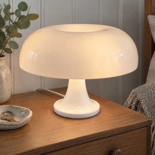 Scandinavian mushroom table lamp lit on a wooden bedside chest against pale panelled walls