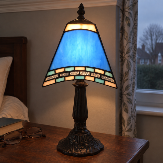 Navy glass shade bedside night light glowing warmly on a dark wooden bedside table