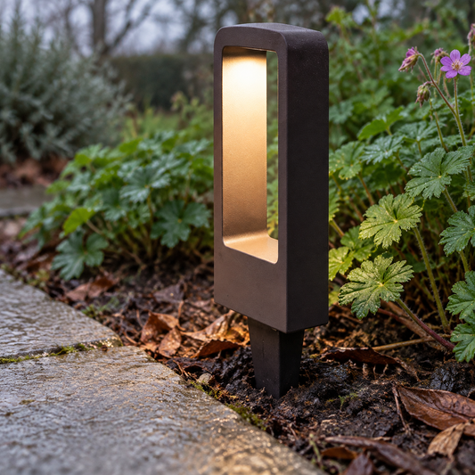 Garden path spike light pushed into damp soil beside a stone path, lit at dusk