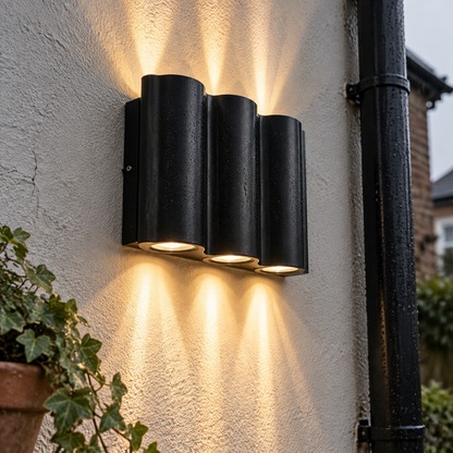 Black aluminium up and down outdoor wall light casting beams on a damp courtyard wall
