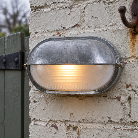 Industrial nautical caged glass outdoor wall lamp lit on weathered painted brickwork