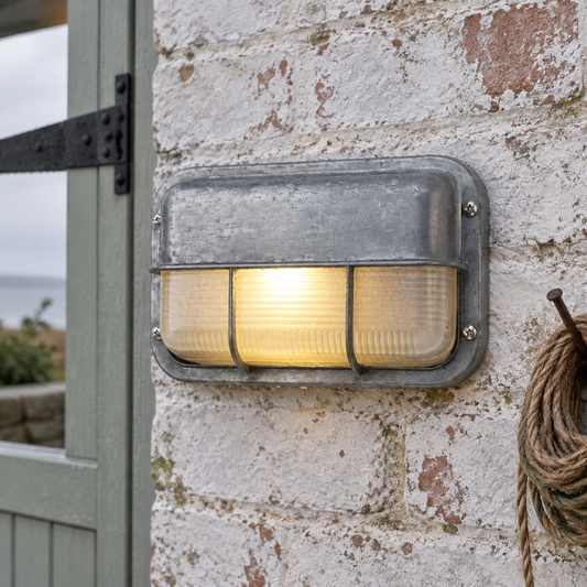 Industrial marine glass outdoor wall sconce lit on whitewashed brick beside a stable door