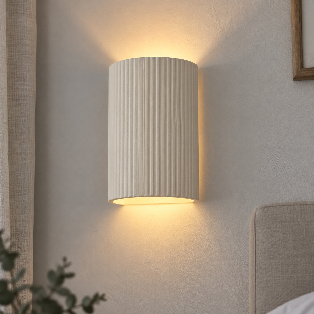Scandinavian beige plaster oval wall sconce lit above a bed on a chalky painted wall