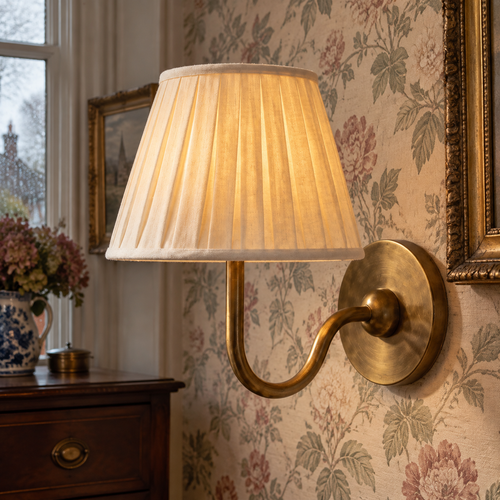 Traditional pleated fabric shade wall sconce lit against floral wallpaper