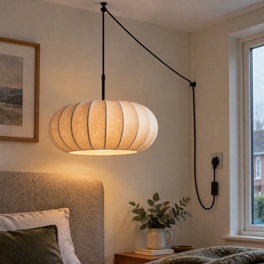 Plug-in pendant light with a fabric shade hanging lit beside a bed headboard
