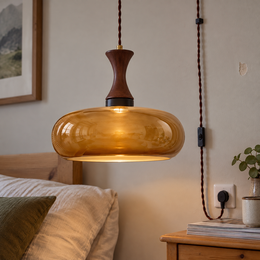 Glass and wood plug-in pendant light hanging lit above a pine bedside chest
