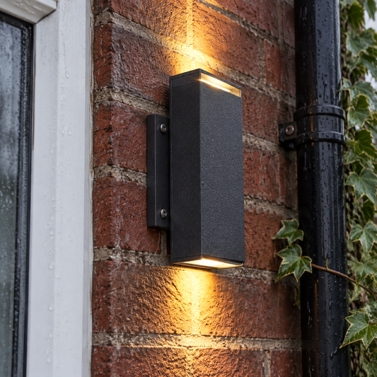 IP67 outdoor LED wall washer light bolted flat to the damp red brick wall of a British house, washing warm light up and down the brickwork on a drizzly afternoon