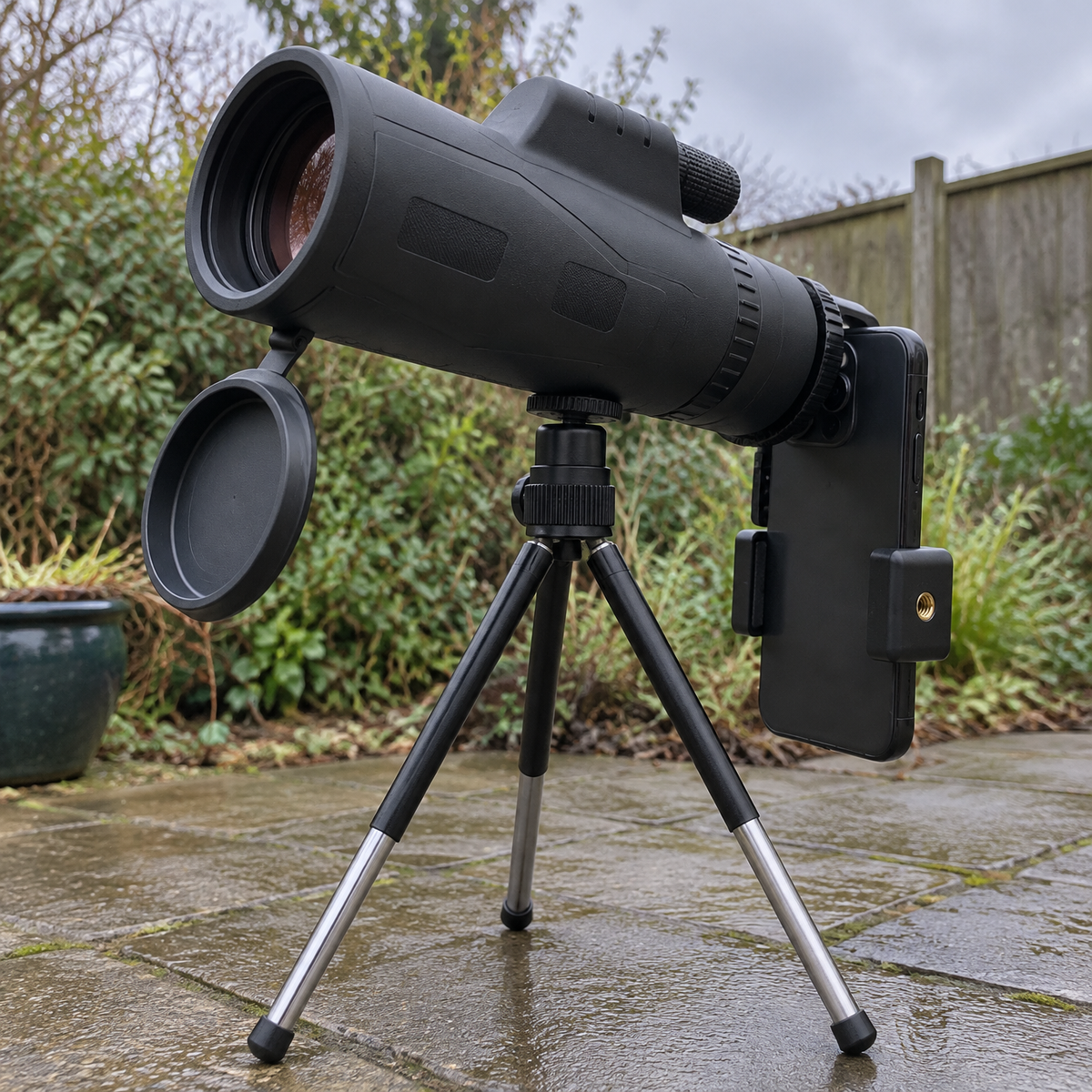 Portable stargazing telescope set up on its tripod on damp patio paving in a British back garden under heavy grey cloud
