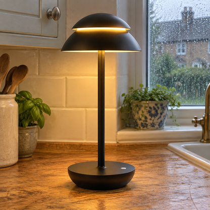 Modern wireless touch table lamp lit on a kitchen worktop with rain on the window behind