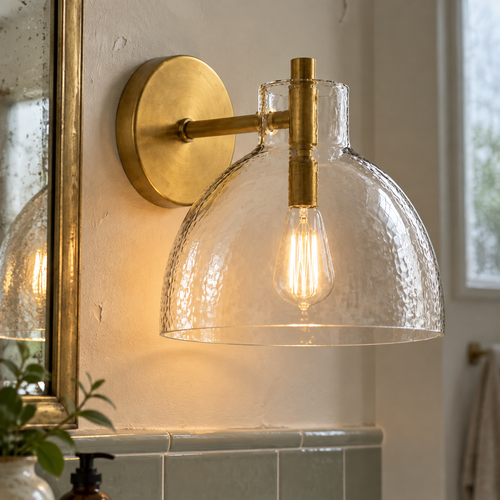 Antique brass recycled glass wall sconce lit beside a bathroom mirror and tiled wall
