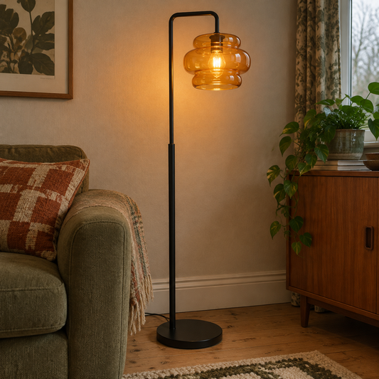Retro black floor lamp with orange glass shade standing lit beside a sitting room sofa