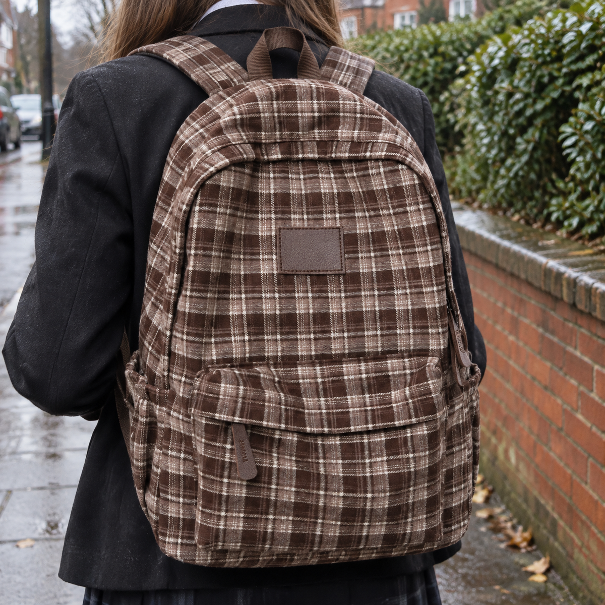 School pupil wearing a checked casual rucksack walking past a brick wall on a drizzly morning