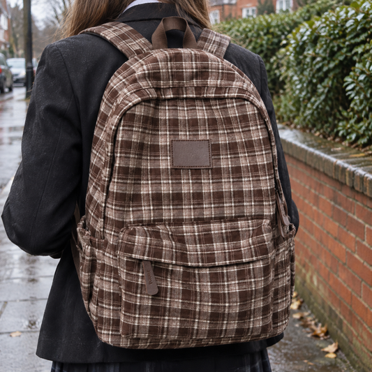 School pupil wearing a checked casual rucksack walking past a brick wall on a drizzly morning