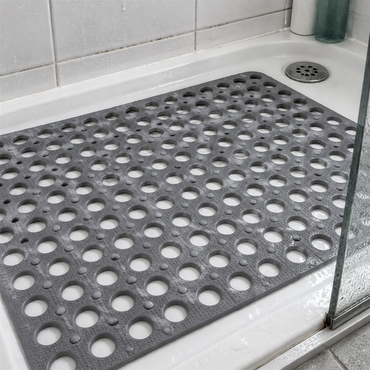 Non-slip bathroom shower mat lying flat in a shower tray beside a chrome drain