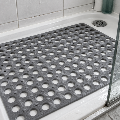 Non-slip bathroom shower mat lying flat in a shower tray beside a chrome drain