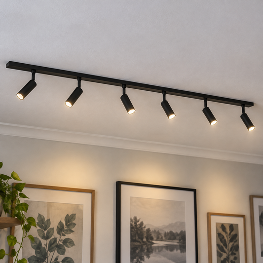 Black slimline track light with six spotlights fixed to a ceiling above a wall of framed prints