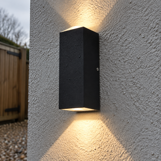 Small up and down wall light casting beams on damp rendered wall beside a timber garden gate