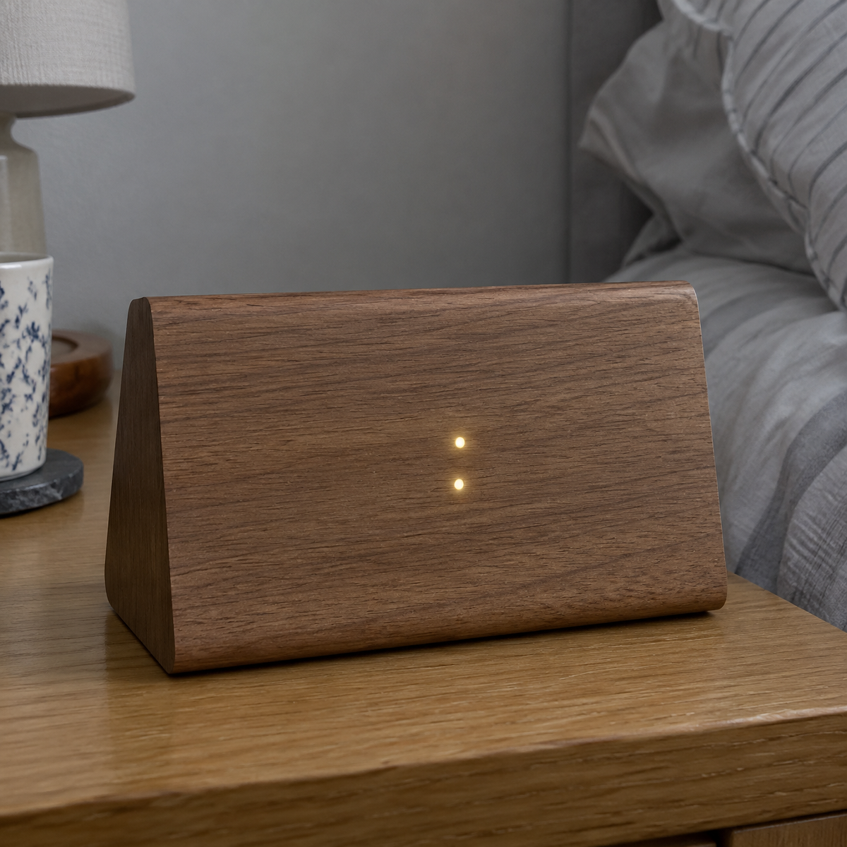 Wooden LED voice control alarm clock glowing dimly on a bedside table beside rumpled bedding