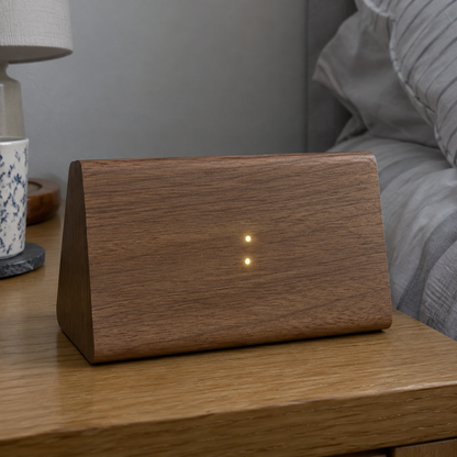 Wooden LED voice control alarm clock glowing dimly on a bedside table beside rumpled bedding