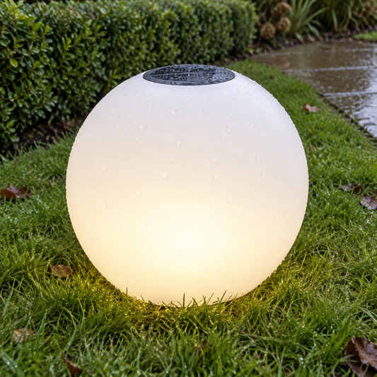 Solar garden globe light glowing in colour on a damp lawn beside clipped hedging