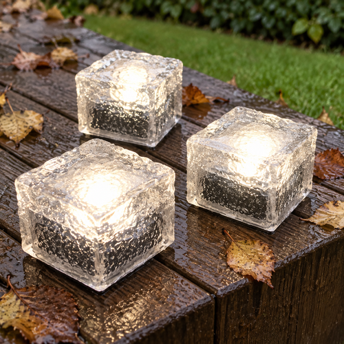 Crystal ice cube solar deck lights sitting on rain-darkened decking boards, glowing warm white among fallen birch leaves