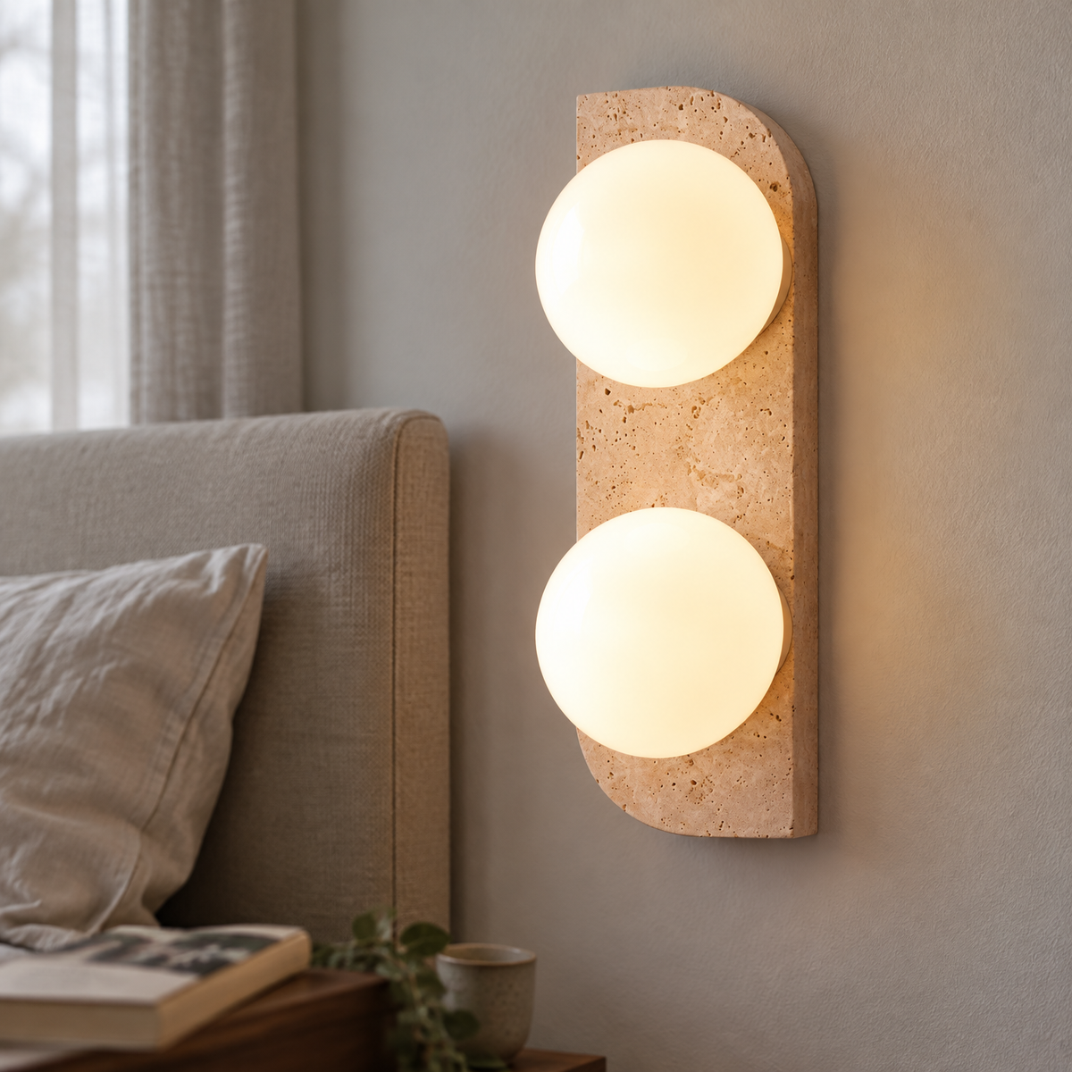 Travertine and white glass bedside wall sconce with its arm projecting over an upholstered headboard in a bedroom