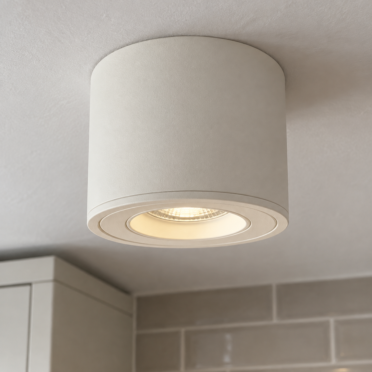 Surface-mounted cylinder ceiling spotlight fixed to a kitchen ceiling, tilted on its gimbal above a wall cupboard