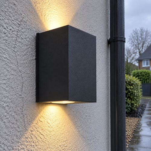 Matte black die-cast aluminium cube outdoor wall light on pale grey render, throwing one beam up and one beam down the wall