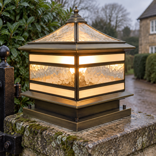 Cast brass and textured glass pillar lantern standing upright on a mossy stone gate pillar beside an iron gate