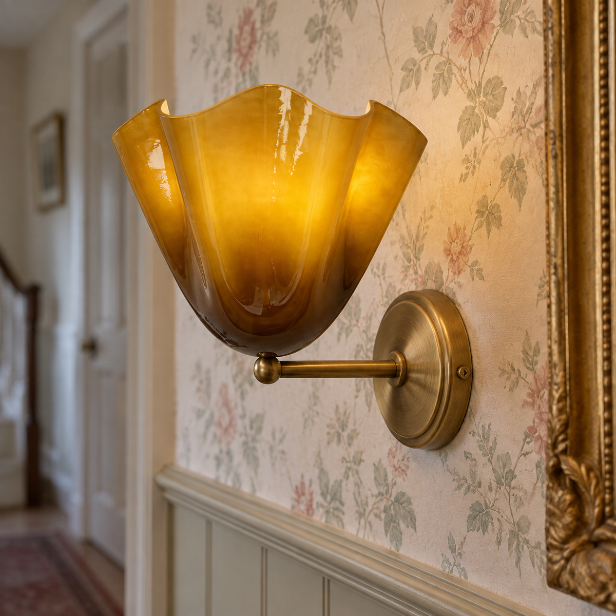 Brass French-style wall sconce with a frosted glass flower shade on a panelled hallway wall beside a gilt mirror