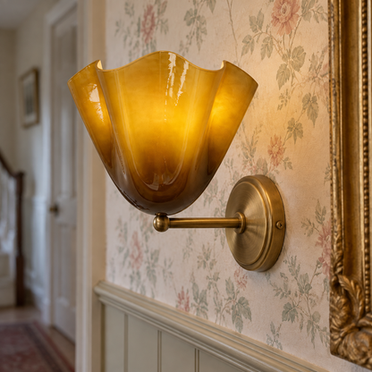Brass French-style wall sconce with a frosted glass flower shade on a panelled hallway wall beside a gilt mirror