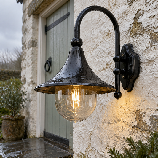 Black barn-style gooseneck outdoor wall light on a whitewashed stone farmhouse wall, wide shade facing down in the rain