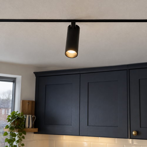 Slim black magnetic track lighting rail on a kitchen ceiling with cylindrical spotlight heads angled at the worktop