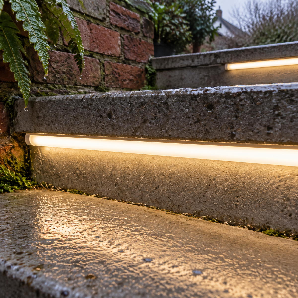 Warm white silicone LED strip fitted under the nosing of wet concrete garden steps, washing light across the treads