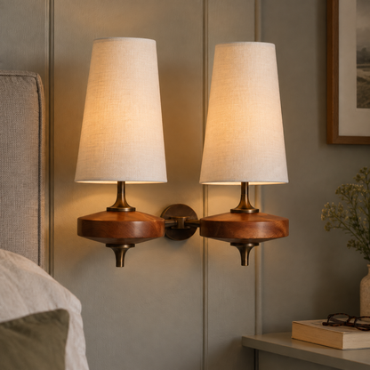 Mid-century walnut wall sconce with a fabric drum shade beside a linen headboard, lit as a warm reading light