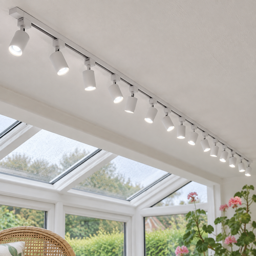 White single-phase track with fourteen white spotlights fixed to a conservatory ceiling beside a glazed roof beam