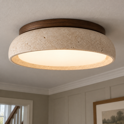 Scandinavian travertine flush-mount ceiling light fitted flat to a hallway ceiling, creamy beige stone disc glowing warmly above white cornicing