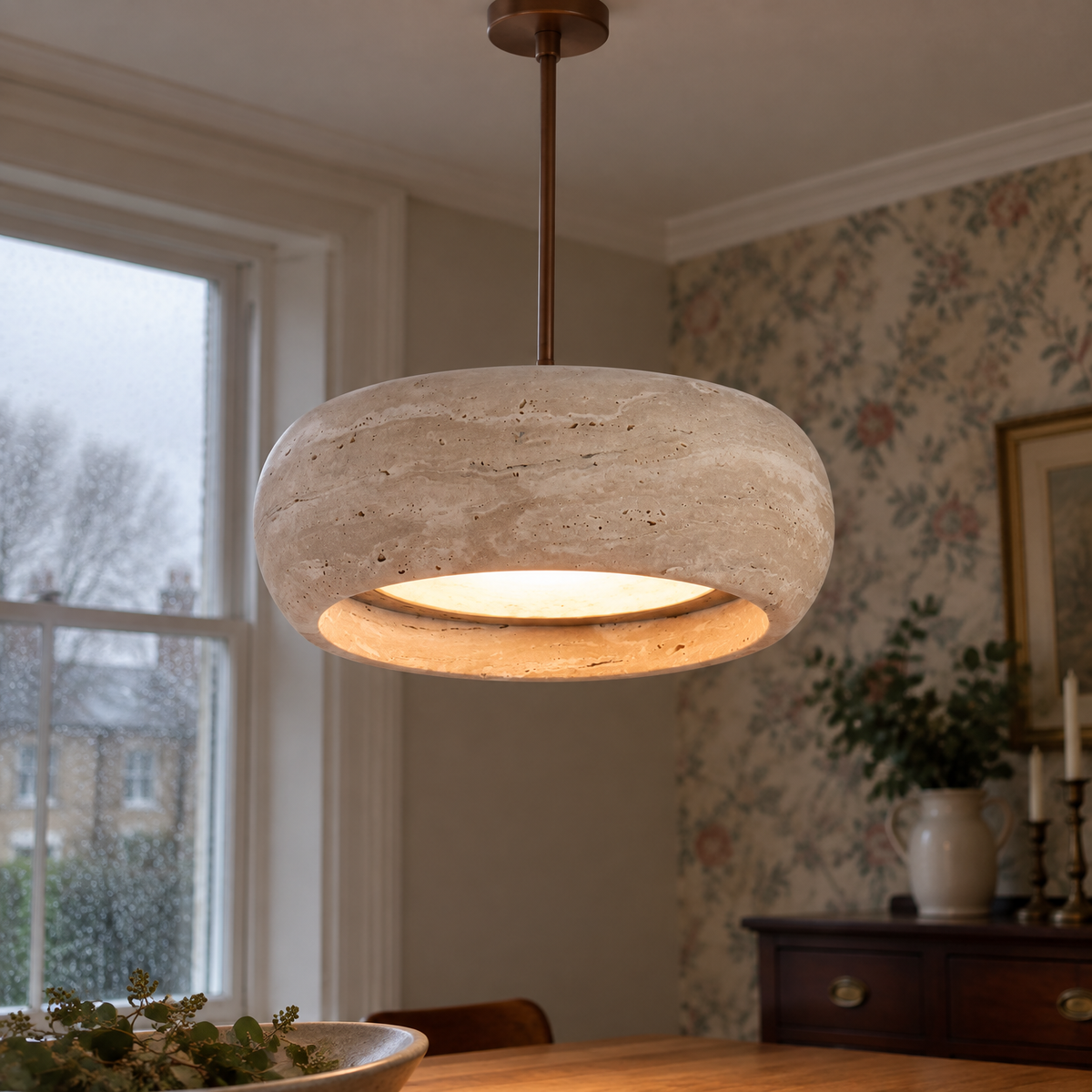 Wide travertine drum pendant light suspended over a dining table, creamy veined stone shade lit above a mahogany sideboard and floral wallpaper