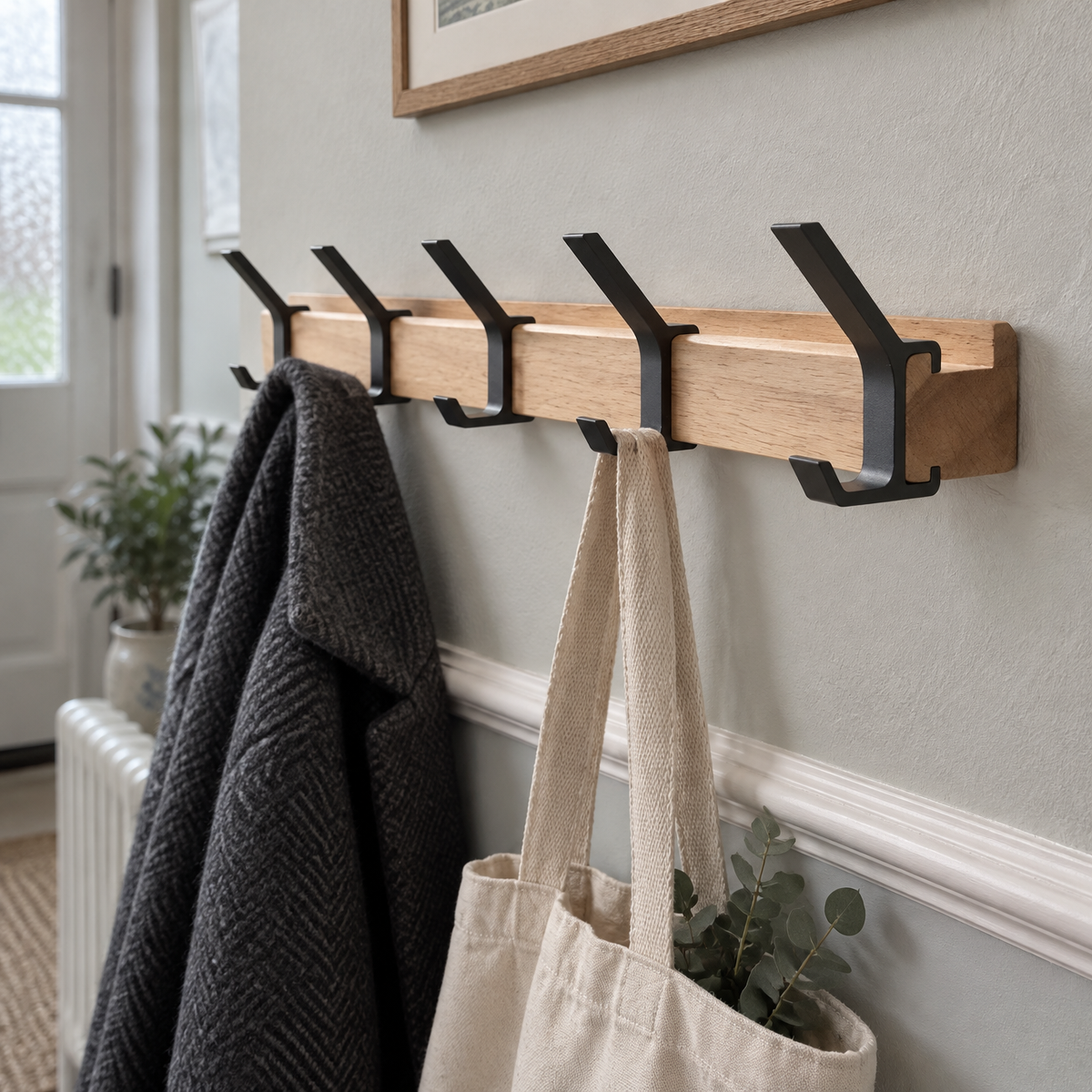 Nordic aluminium wall coat rack mounted level in a hallway with a wool coat and canvas tote hanging from its hooks