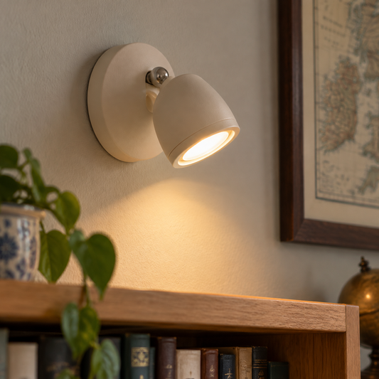 Remote control wall spotlight stuck to a study wall above a bookshelf, adjustable head angled down onto the book spines