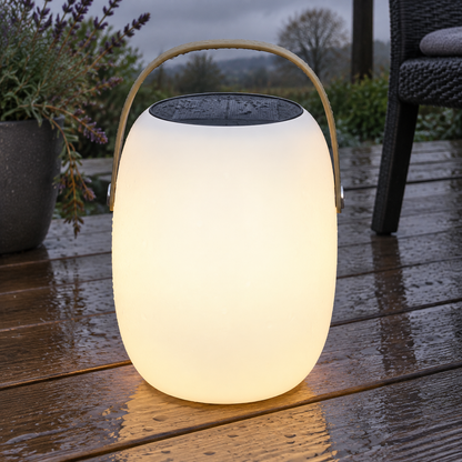 White portable solar floor lantern standing upright on damp decking beside a pot of lavender at overcast dusk