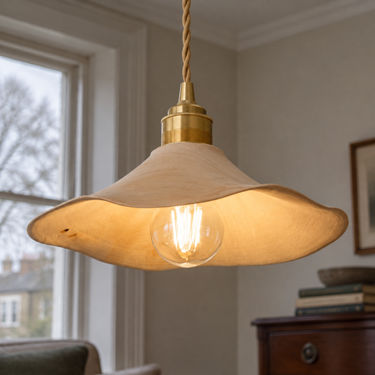 Wabi-sabi wood and brass pendant light hanging in a sitting room above a mahogany dresser and stack of books